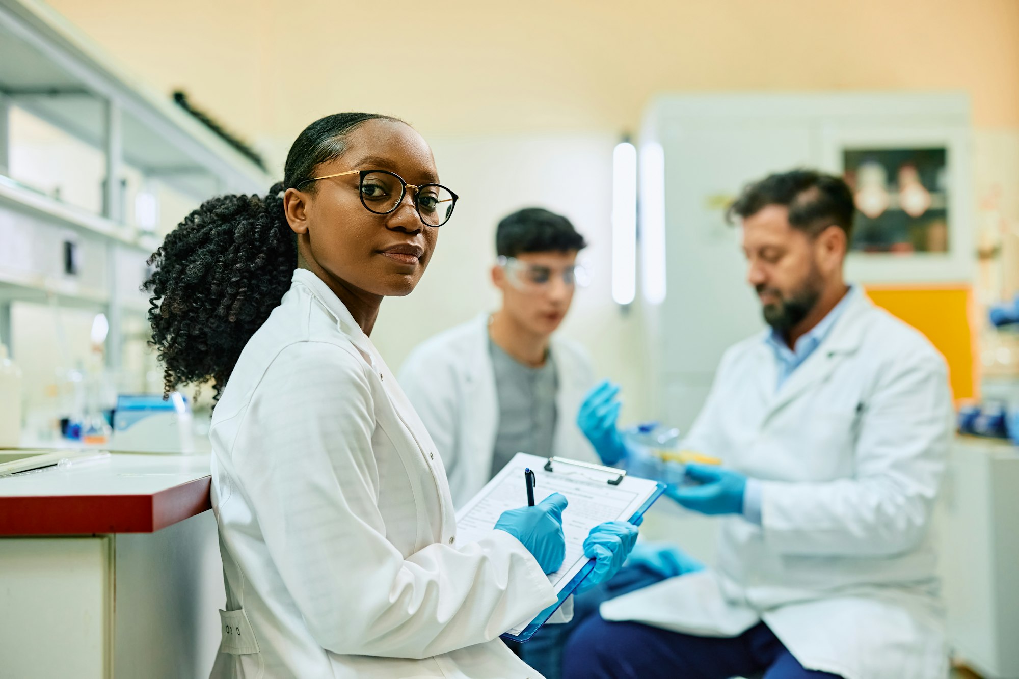 Black female scientist writing notes during a research in laboratory and looking at camera.